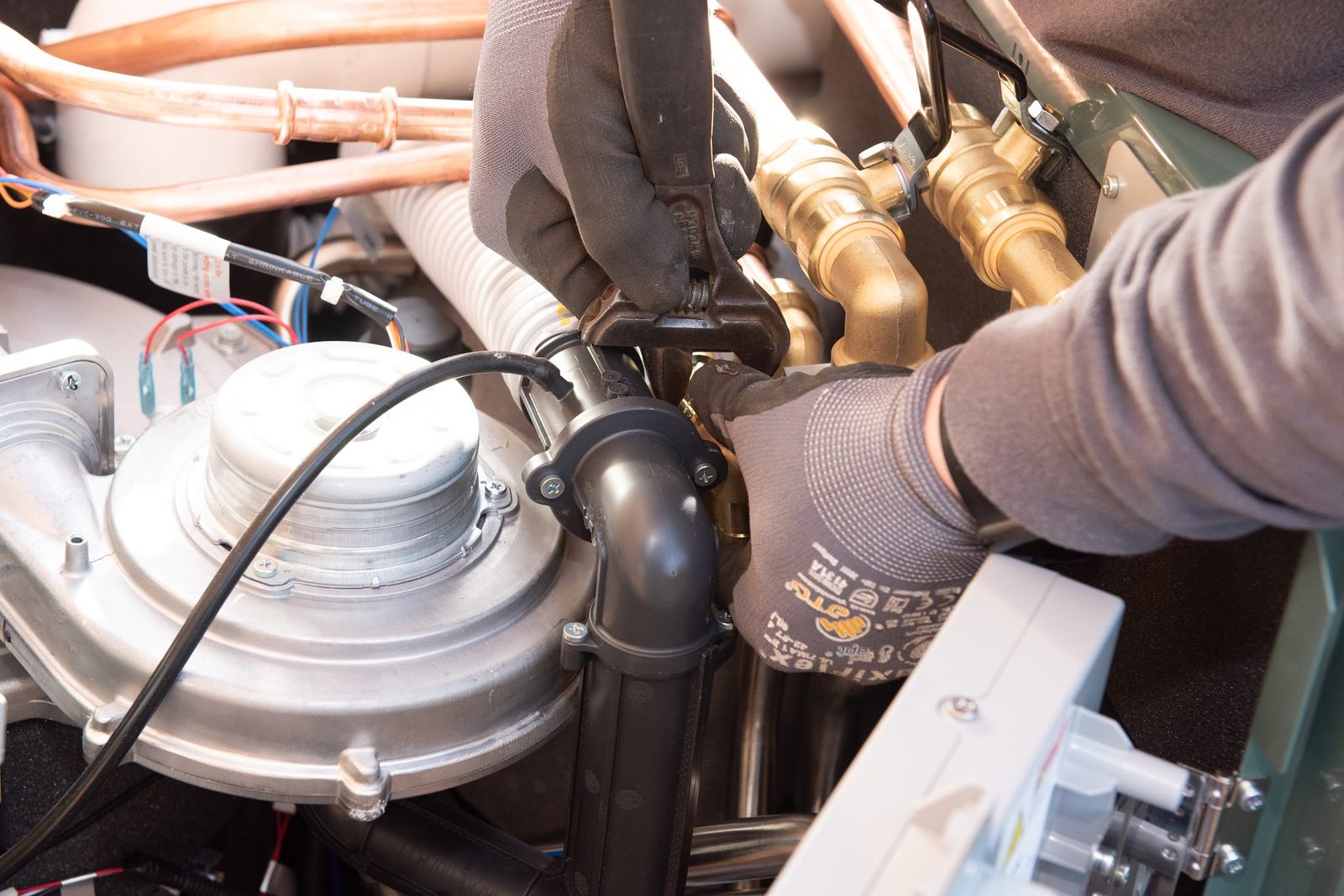 Gloved hands working on a boiler fan and burner assembly